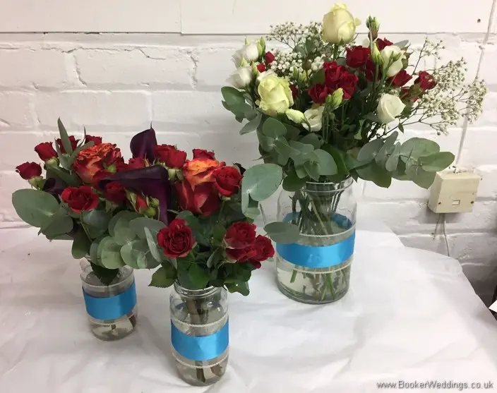 Table Centrepiece decorations of orange, raspberry & dark red coloured bouquet with roses, spray roses, lissianthus and calla lillies