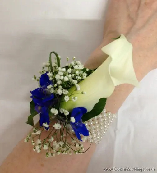 White calla lily, blue delphinium and gypsy grass wrist corsage on a pearl bracelet shown on the wrist